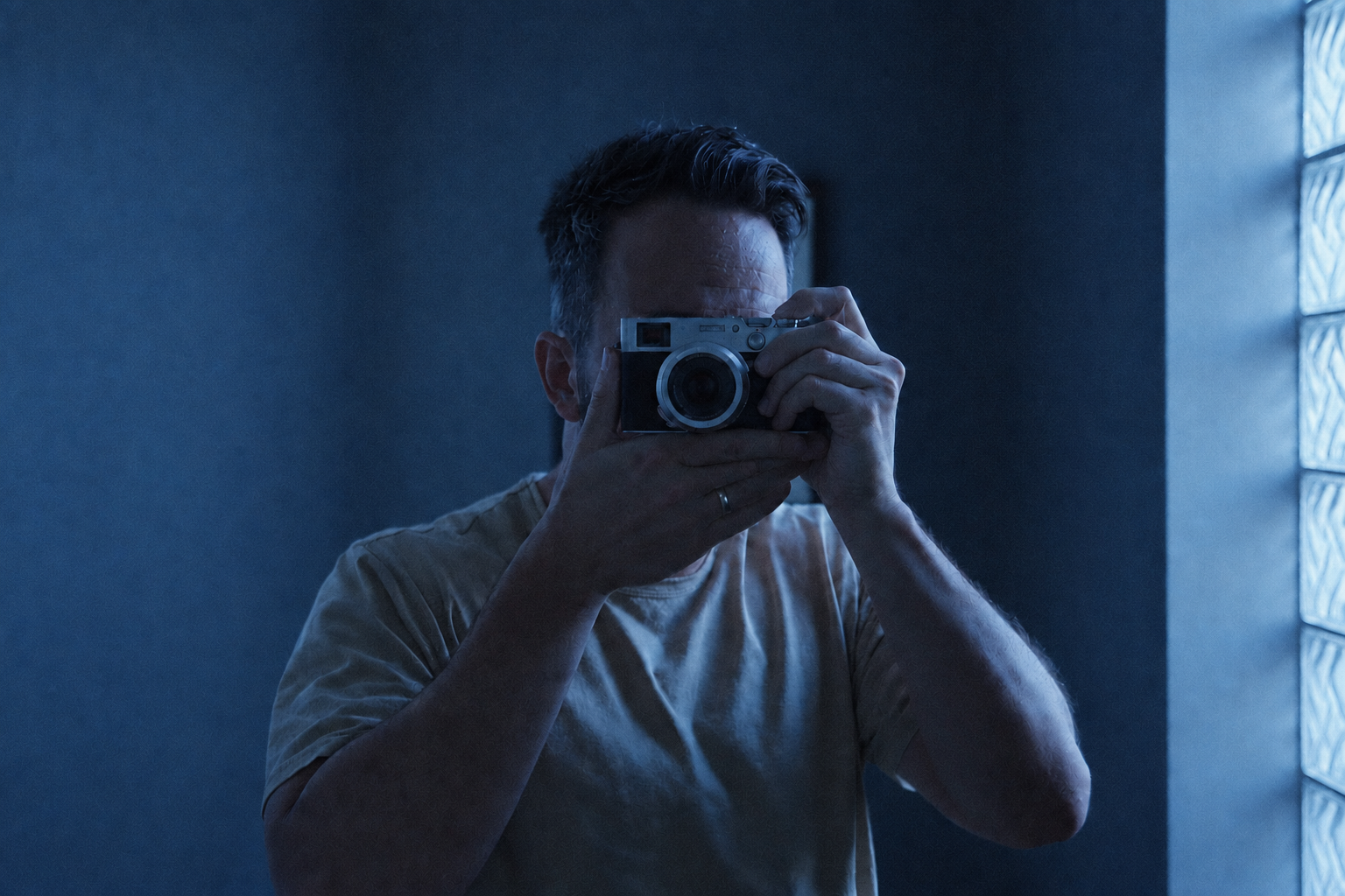 Photographer making a self-portrait with a compact camera in soft blue window light
